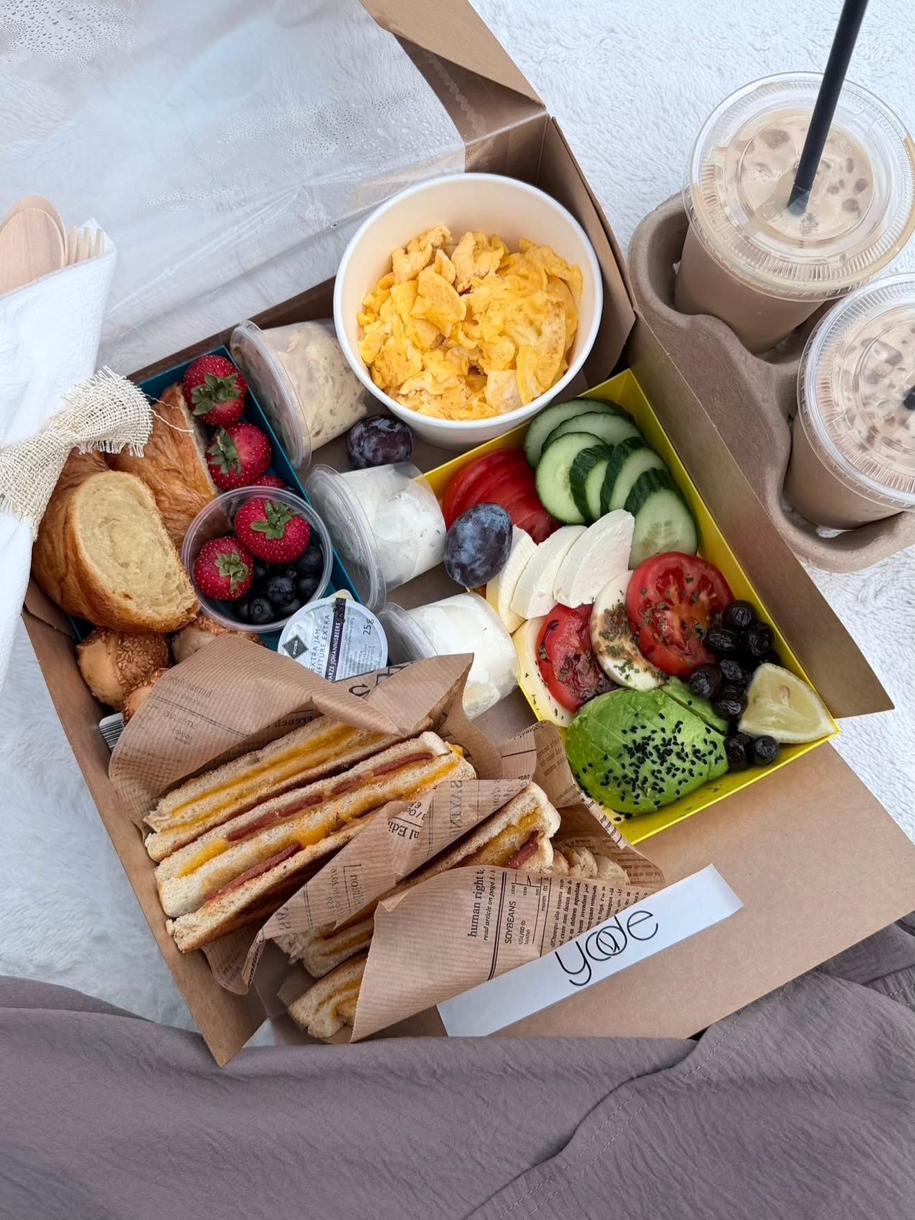 Geöffnete Café-Yade-Picknickbox mit Sandwiches, Obst und Dips am Wasser